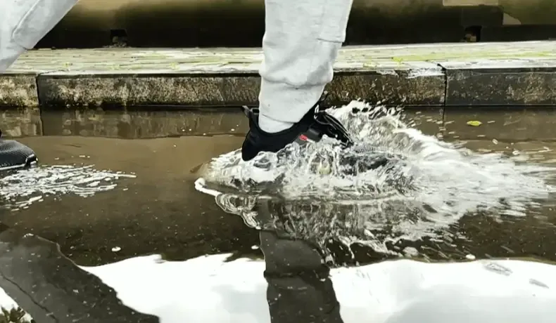 Black shoes splashing through a puddle in rain